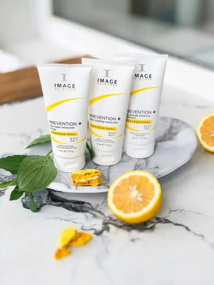 Three skincare tubes arranged on a marble surface with lemon halves and green leaves